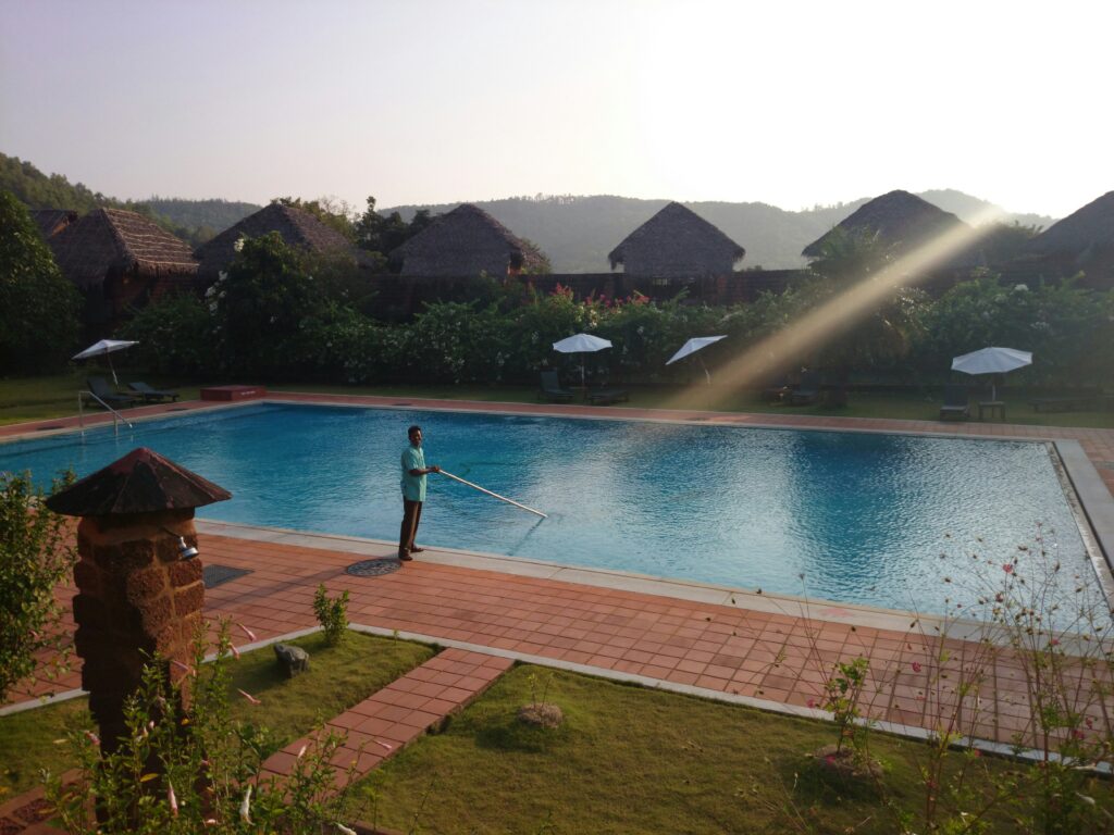 Pool cleaning professional maintaining a sparkling clear swimming pool surrounded by lush greenery and lounge chairs, emphasizing the importance of pool service businesses in tax compliance.
