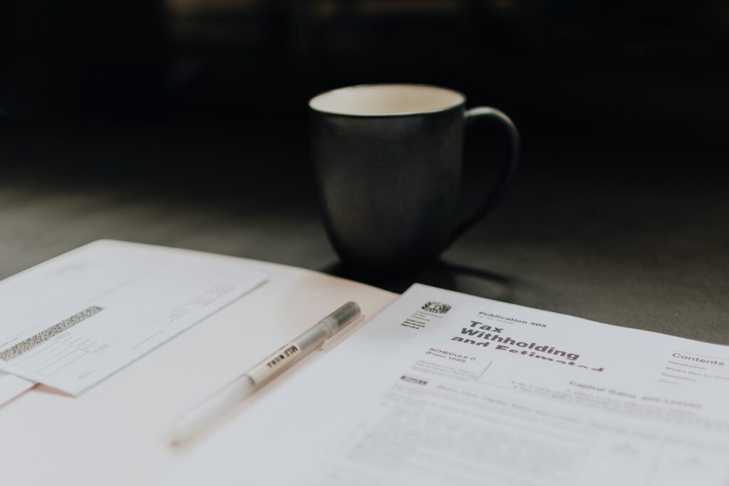 Tax withholding documents and a pen on a desk with a coffee cup, illustrating worker classification and tax obligations for W-2 employees and 1099 independent contractors.