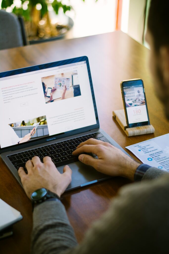 Person using a laptop to access online resources for filing 1099 forms, smartphone displaying financial information, workspace setup for freelancers and gig workers.