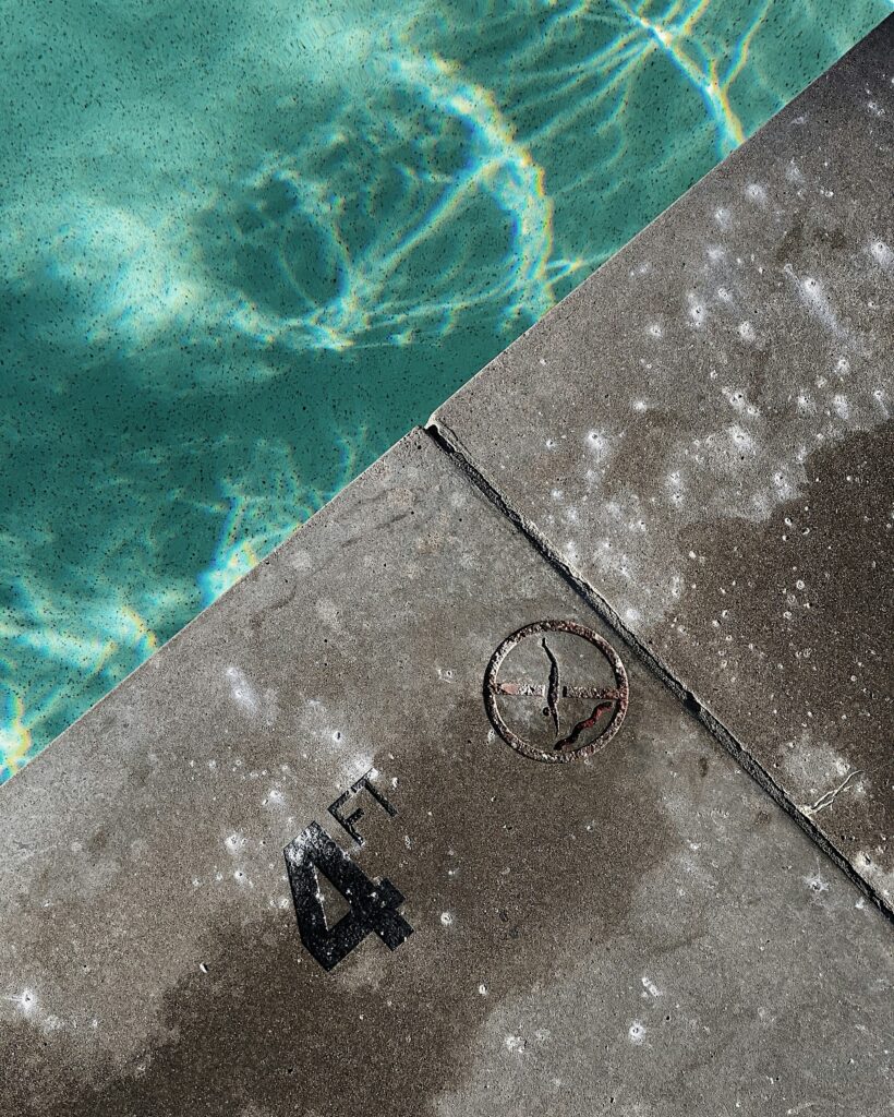 Poolside view showing the water's surface and a concrete edge marked with "4 FT" and a circular drain cover, relevant to pool maintenance and cleaning services.