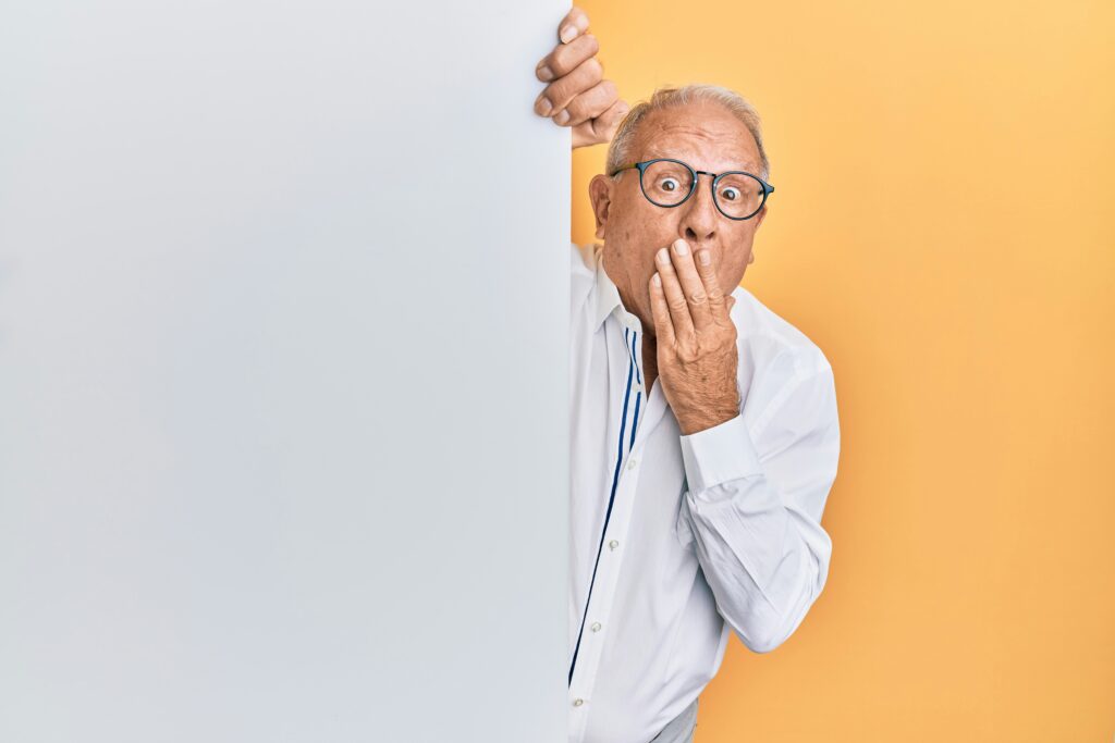 Surprised elderly man in a white shirt and glasses, covering his mouth, appearing anxious about filing an incorrect 1099 form.