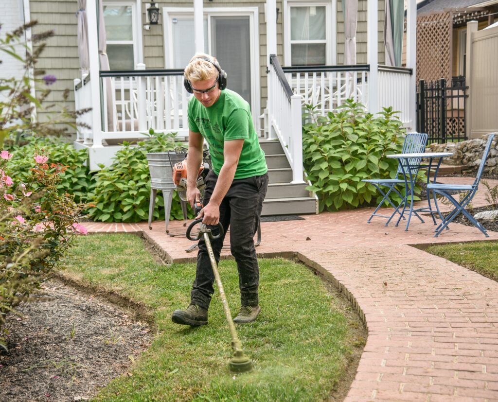 Landscaper using a string trimmer in a residential garden, emphasizing the importance of 1099 filing for landscaping businesses.