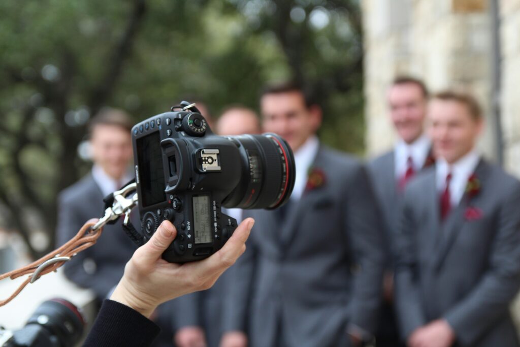 Camera held by a photographer capturing a group of groomsmen in formal attire, emphasizing the role of photography in event planning and the creative industry.