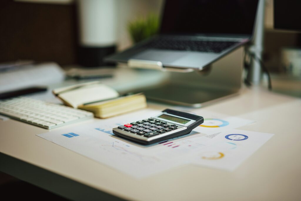 Calculator on a desk with financial documents and a laptop, illustrating the importance of 1099 e-filing software for small business owners.